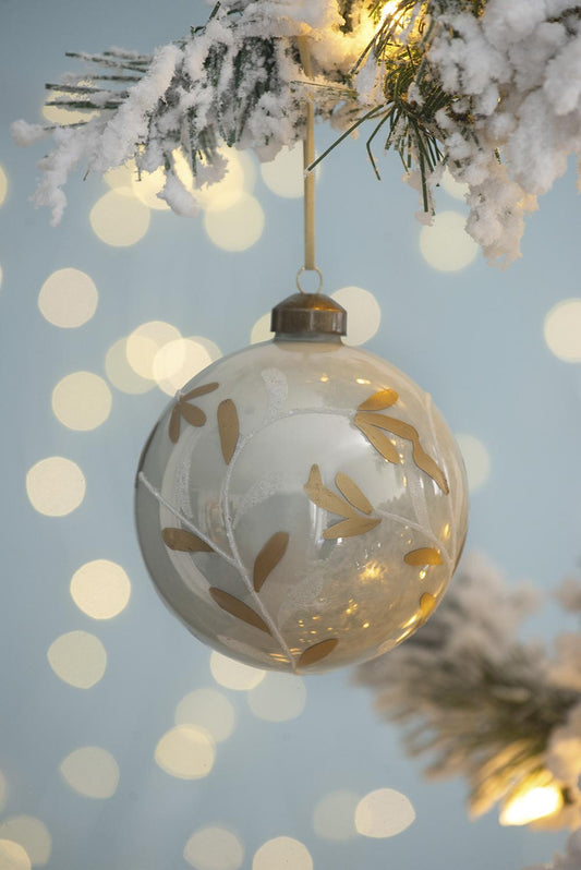 Glass Christmas bauble with gold leaf design hanging from a frosted pine branch