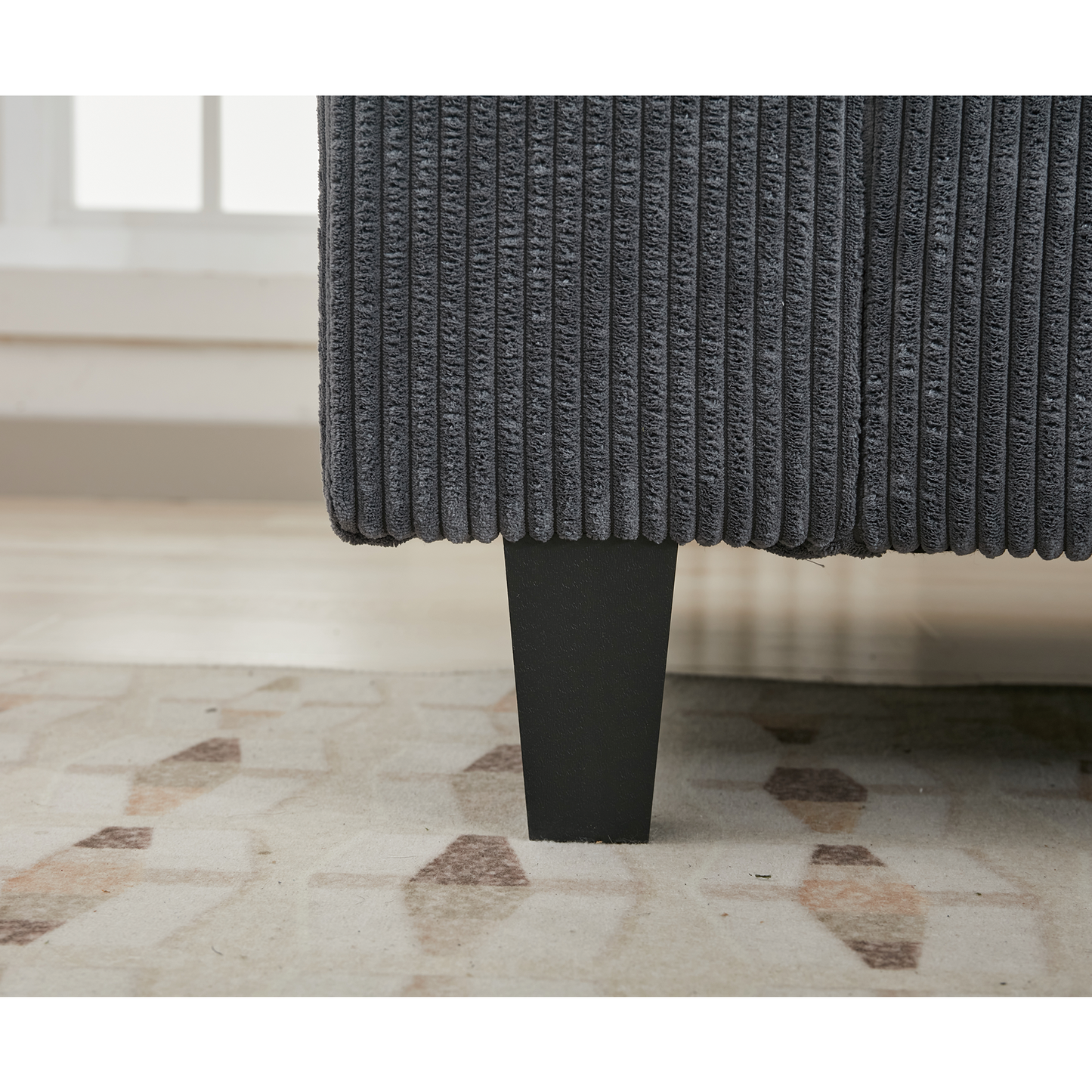 Closeup of a dark gray corduroy sofa leg with a modern tapered design on a geometric rug
