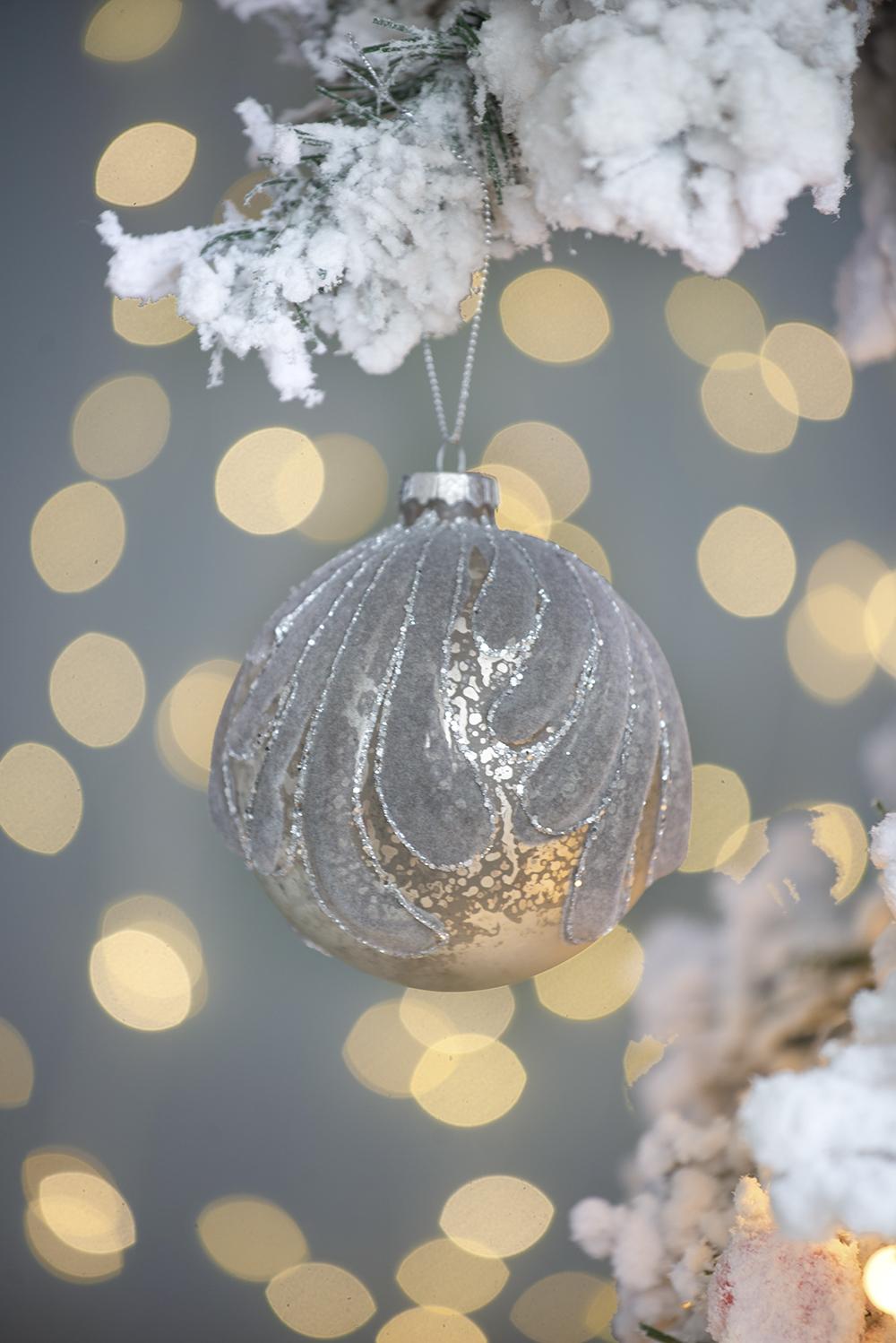 Elegant silver Christmas ornament with swirling textured pattern hanging on a snowy branch