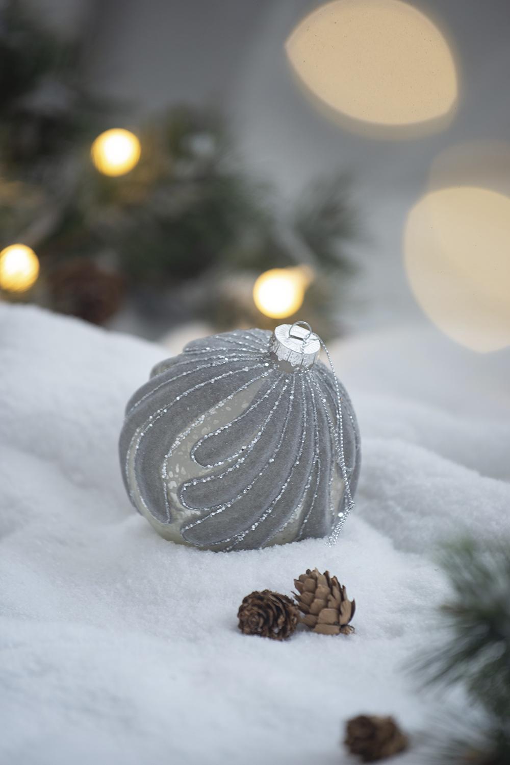 Sparkling silver spiral Christmas ornament with a frosted glass finish resting on snow