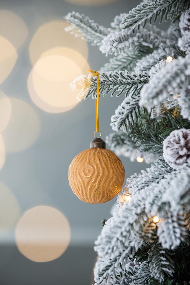 Golden woodgrain Christmas ornament hanging on a flocked tree branch