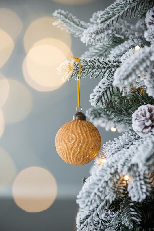 Golden woodgrain Christmas ornament hanging on a flocked tree branch