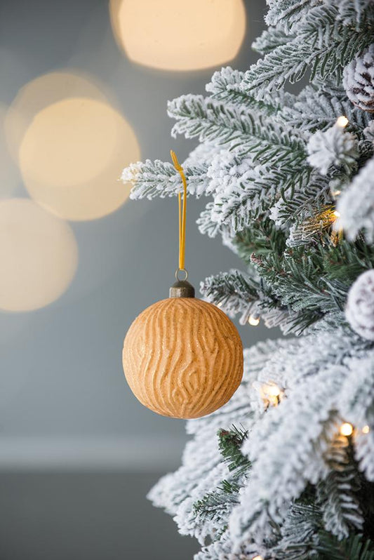 Wood grain textured round Christmas ornament hanging on a flocked pine tree