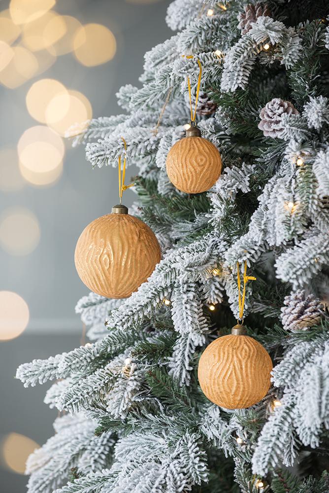Textured orange walnutshaped Christmas ornaments hanging on a flocked tree