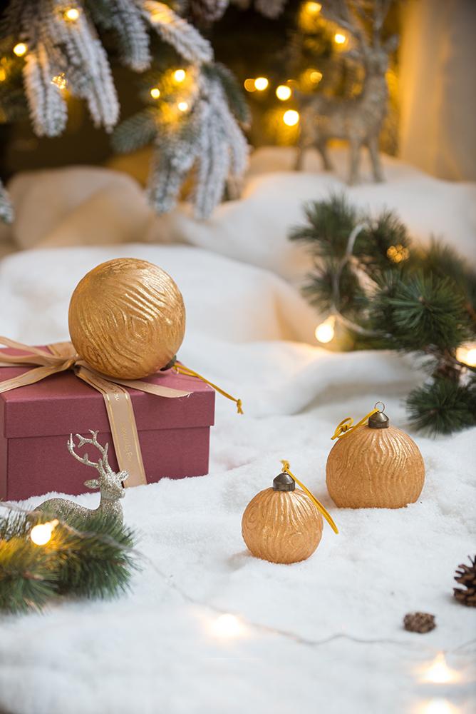 Textured golden Christmas ornaments with brown ribbon accents on white snow