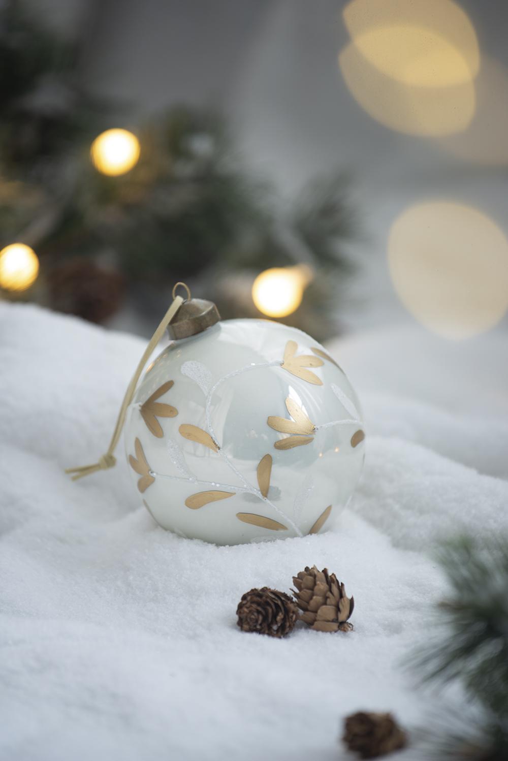 White glass Christmas ornament with gold floral accents on snow