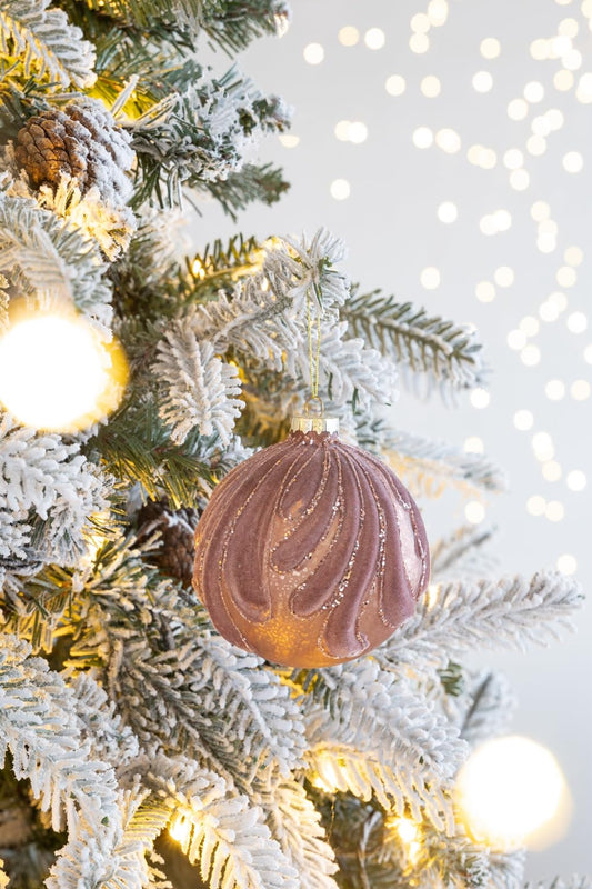Rose gold glitter swirl Christmas ornament hanging on a flocked tree with bokeh lights