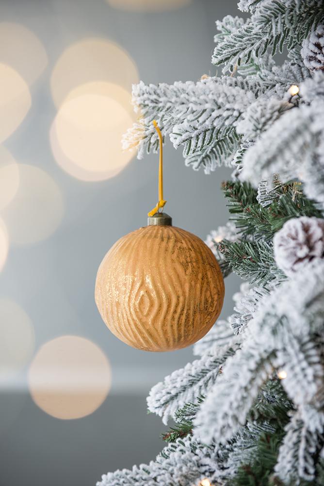 Gold woodgrain Christmas ornament hanging on a frosted tree branch