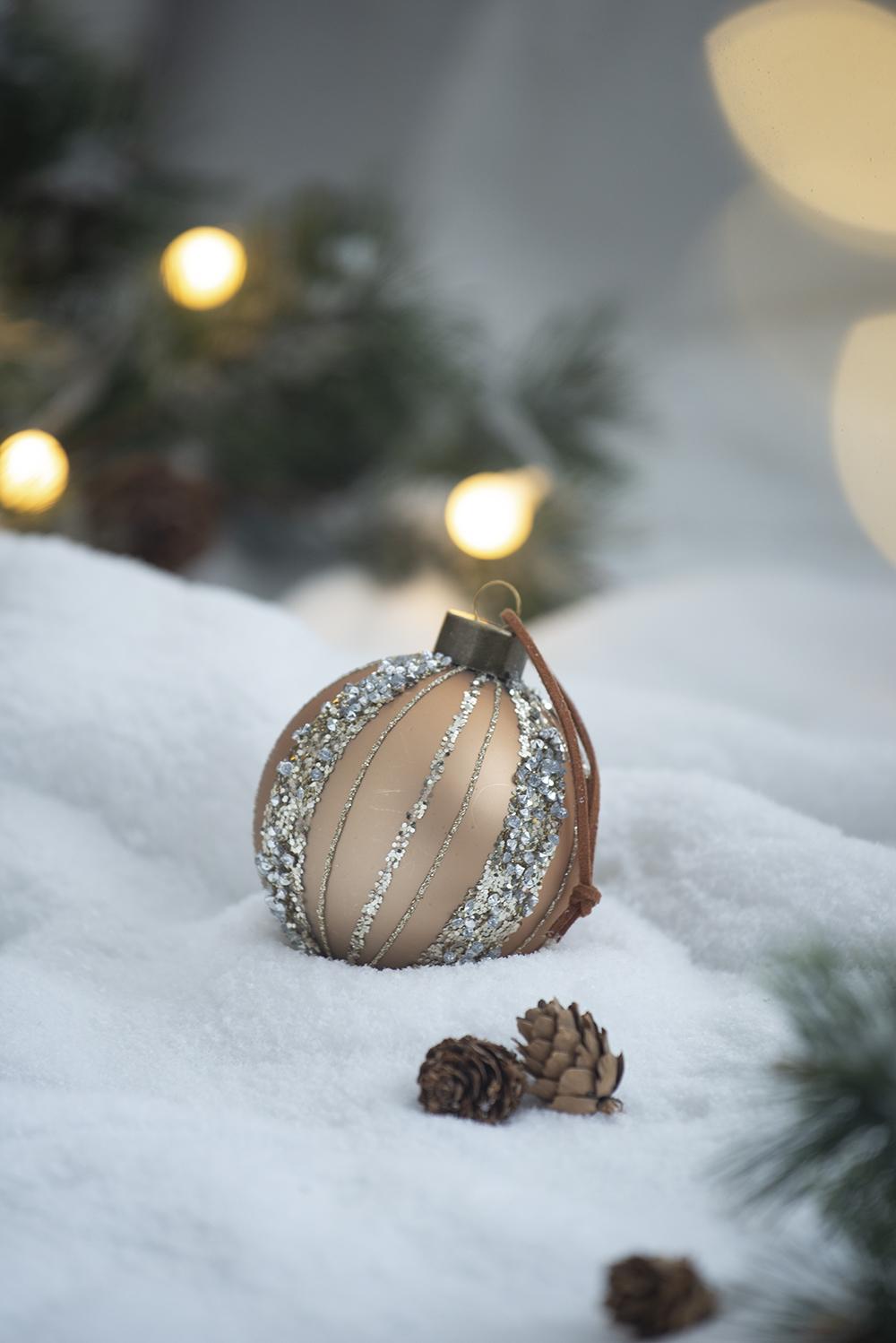 Champagne Christmas ornament with glitter accents on white snow