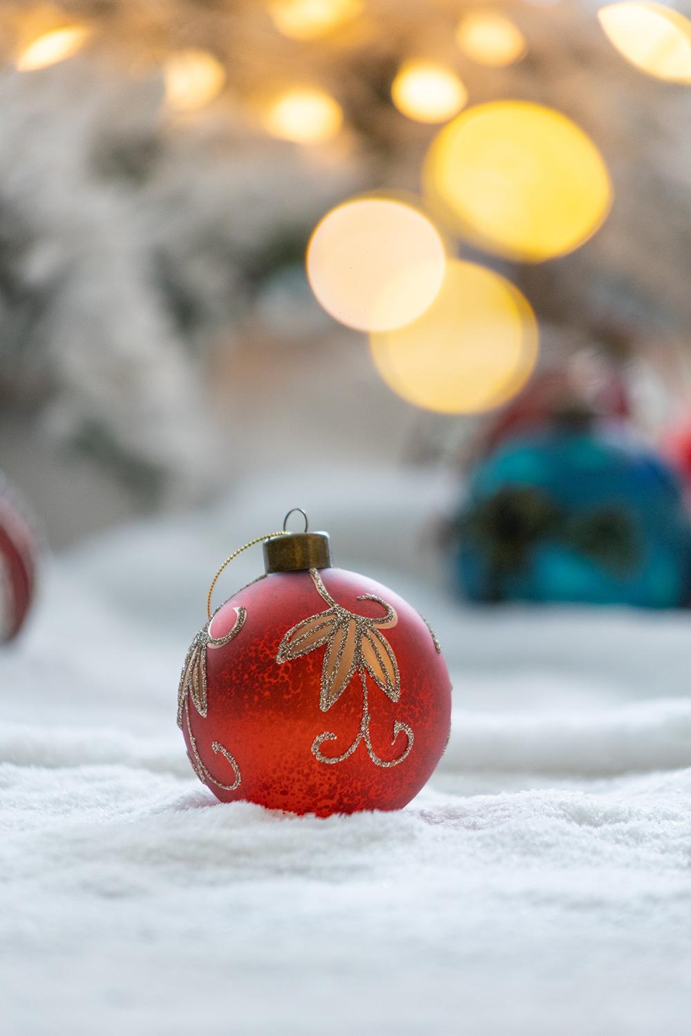 Shiny red glass Christmas ornament with gold filigree pattern resting in faux snow