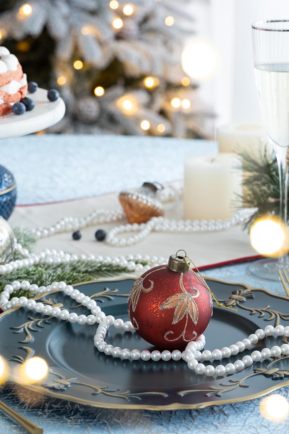 Red glass Christmas ornament with gold leaf design on a dark blue plate