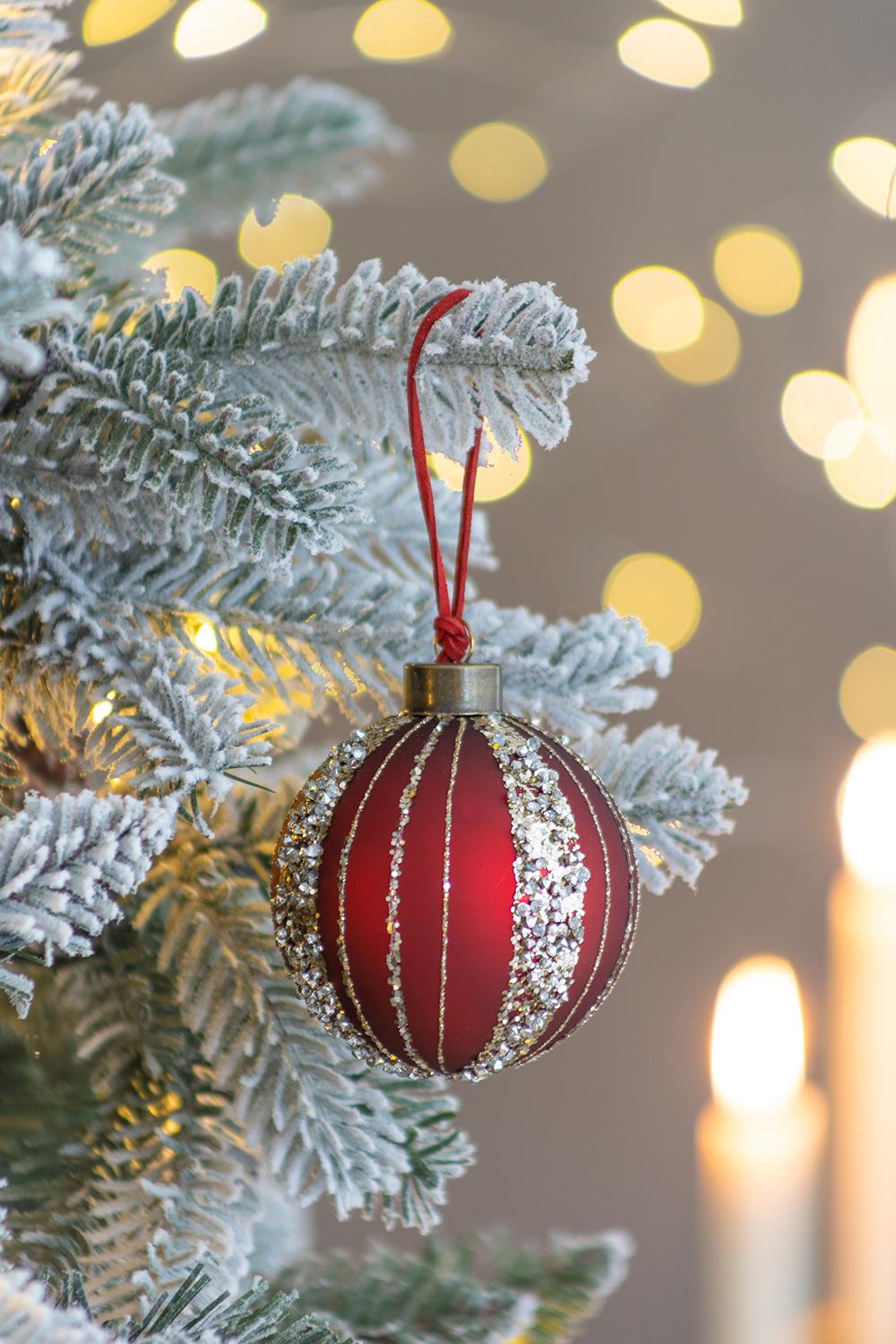 Red glass Christmas ornament with silver glitter stripes hanging on a flocked tree branch