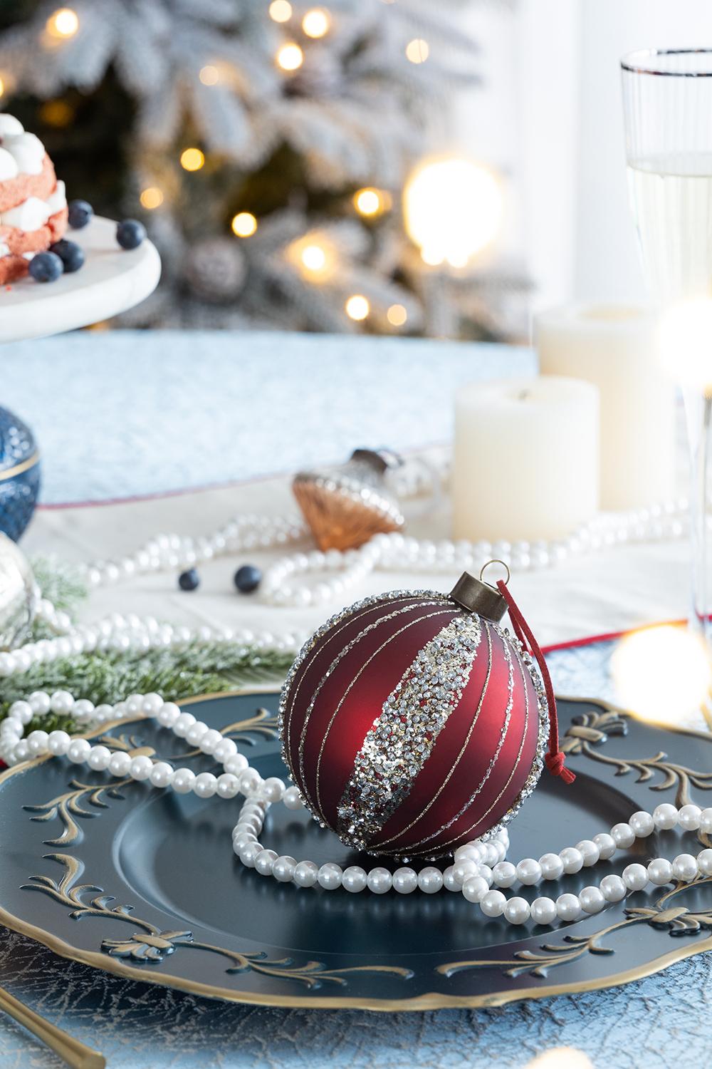 Red glass Christmas ornament with glitter accents resting on a dark blue plate