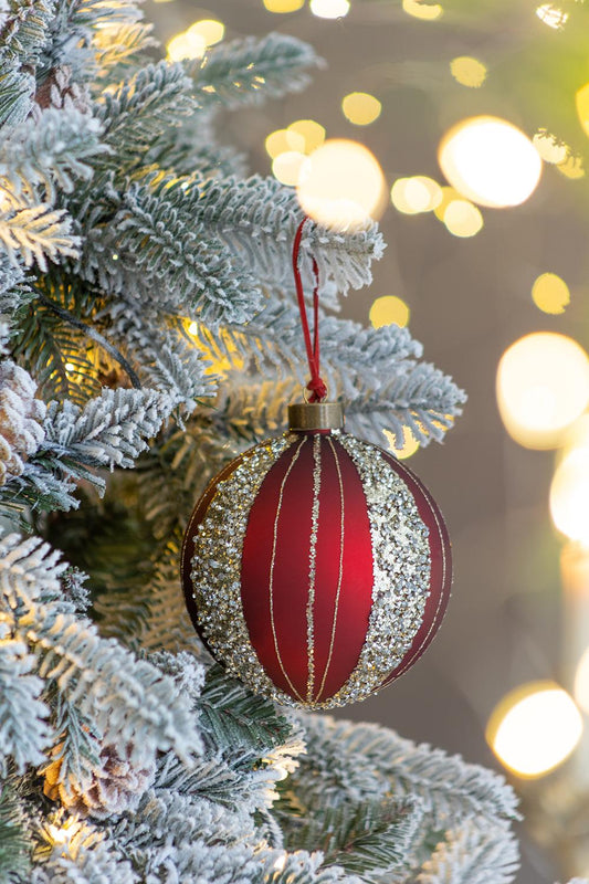 Red striped glass Christmas ornament with glitter accents hanging on a frosted tree branch