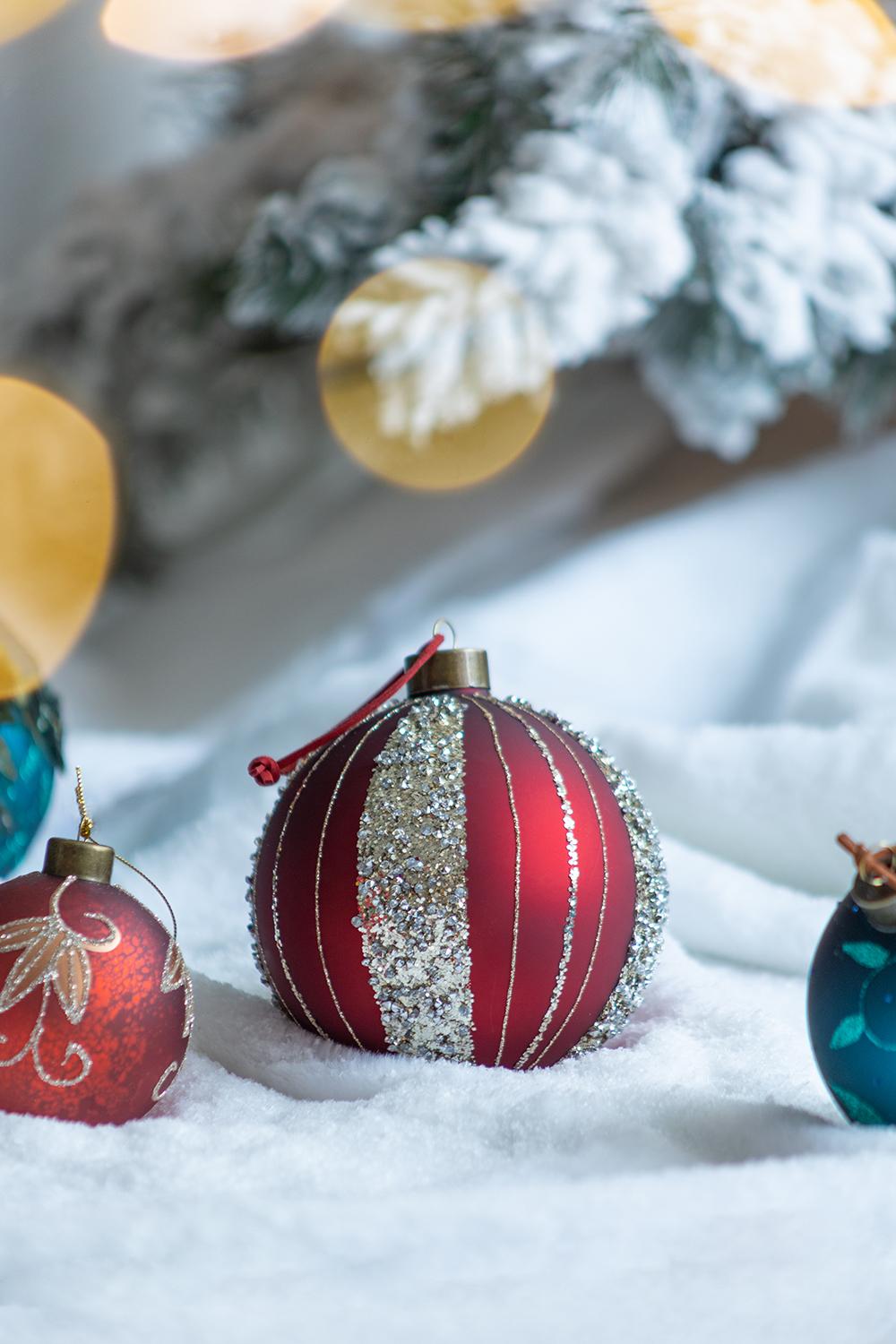 Red striped Christmas ornament with glitter accents on a snowcovered branch