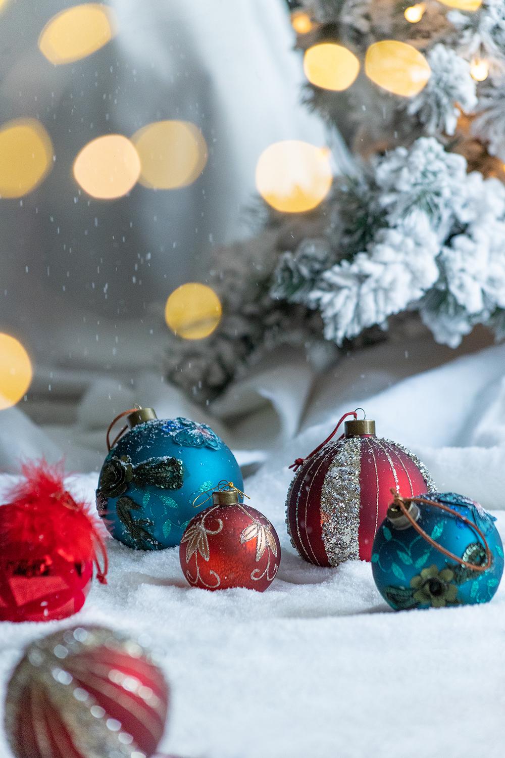 Festive red and blue Christmas ornaments scattered on snow with bokeh lights