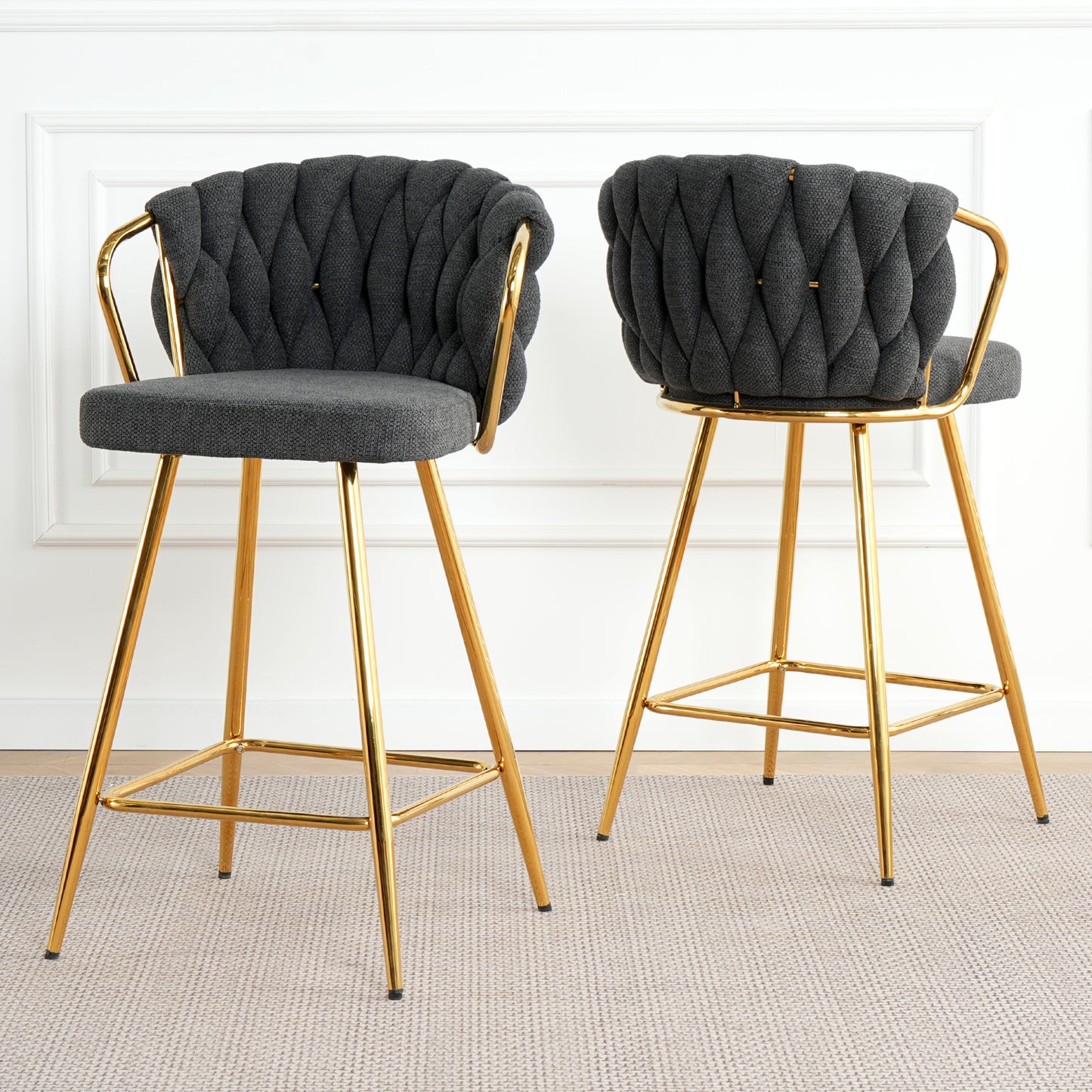 Two dark gray tufted bar stools with gold metal legs are shown in a bright modern setting