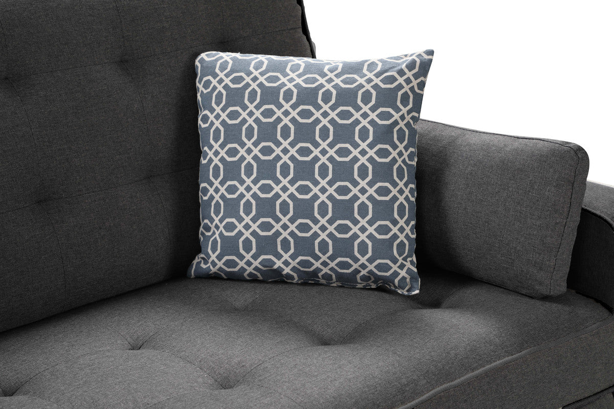 Blue geometric throw pillow with white interlocking pattern on a charcoal grey tufted sofa