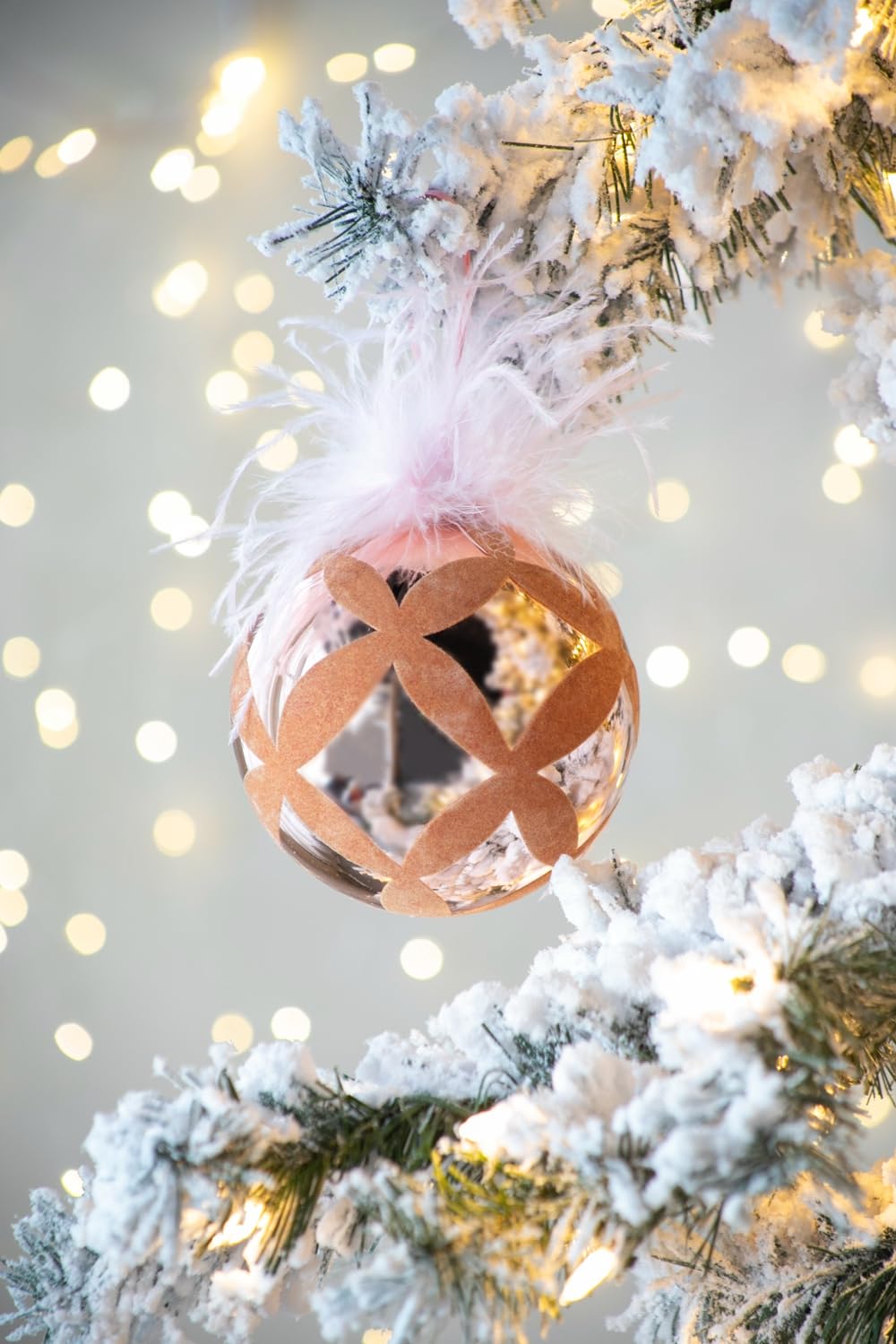 Elegant rose gold Christmas ornament with feather accent on frosted tree branch