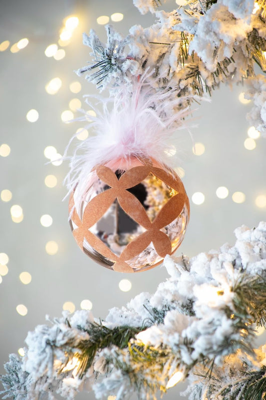 Elegant rose gold Christmas ornament with feather accent on frosted tree branch