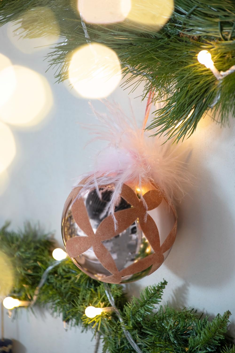 Rose gold Christmas ornament with floral cutouts and feather accents