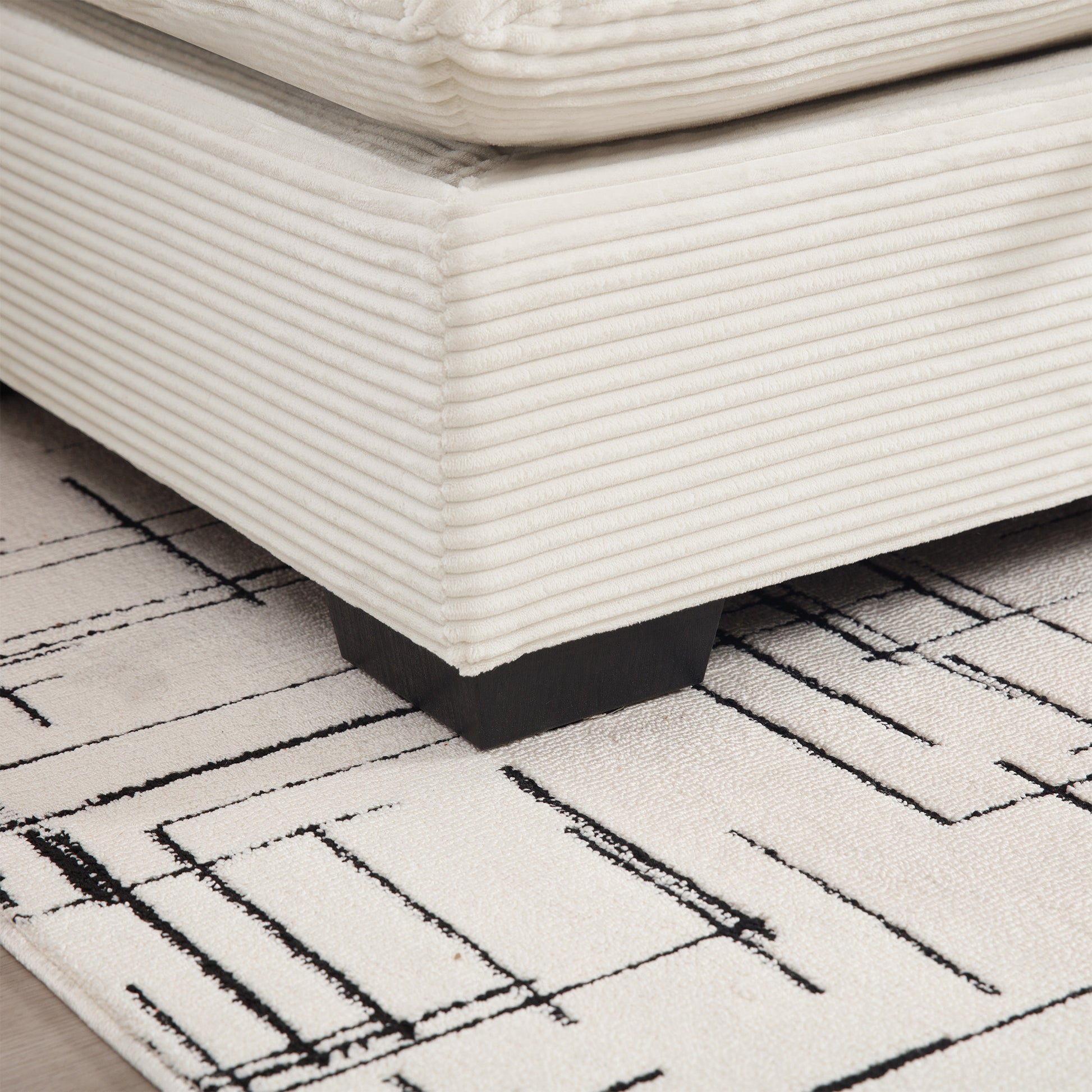 Cream corduroy ottoman corner with black wooden leg rests on a black and white geometric rug
