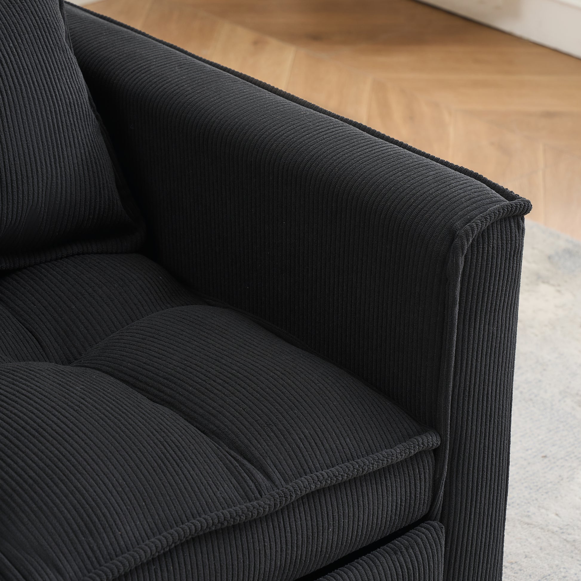Closeup of plush black corduroy sofa armrest with tufted seat cushion detail