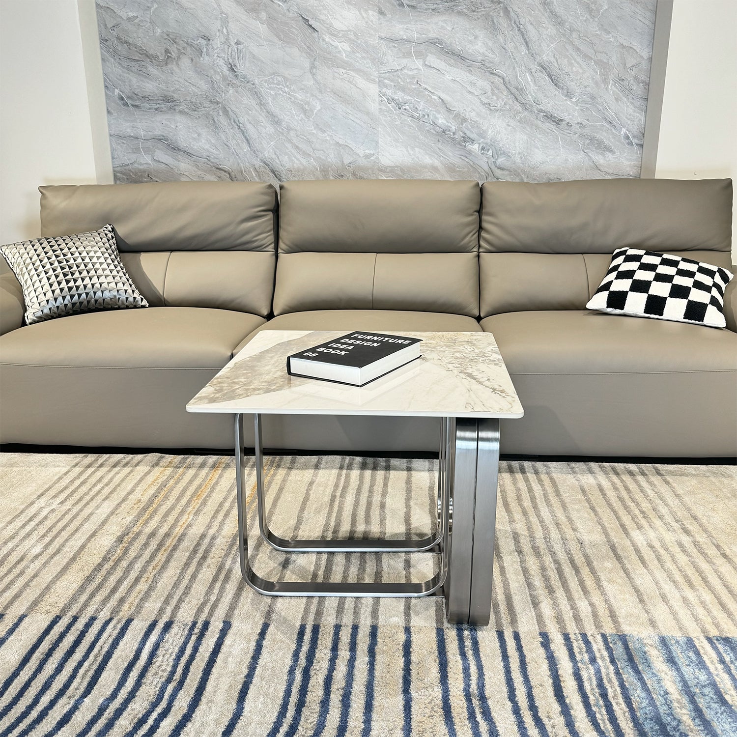 Modern light grey leather seater sofa with decorative pillows and a marbletop side table