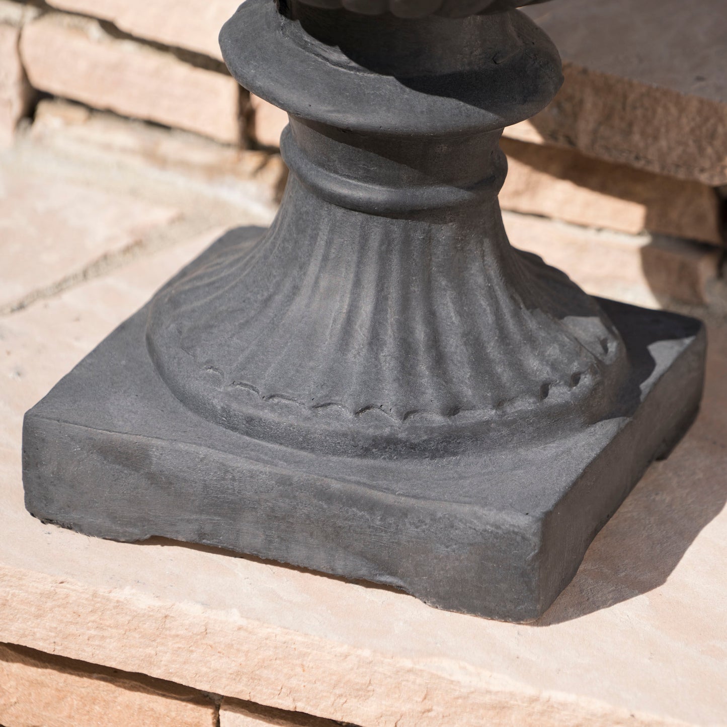 Dark gray cast iron urn base with fluted detailing providing a sturdy foundation for garden decor