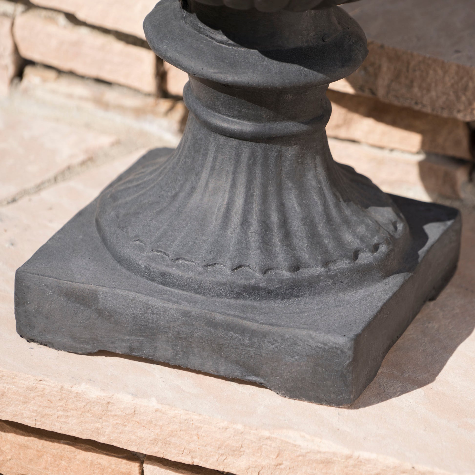 Dark gray cast iron urn base with fluted detailing providing a sturdy foundation for garden decor