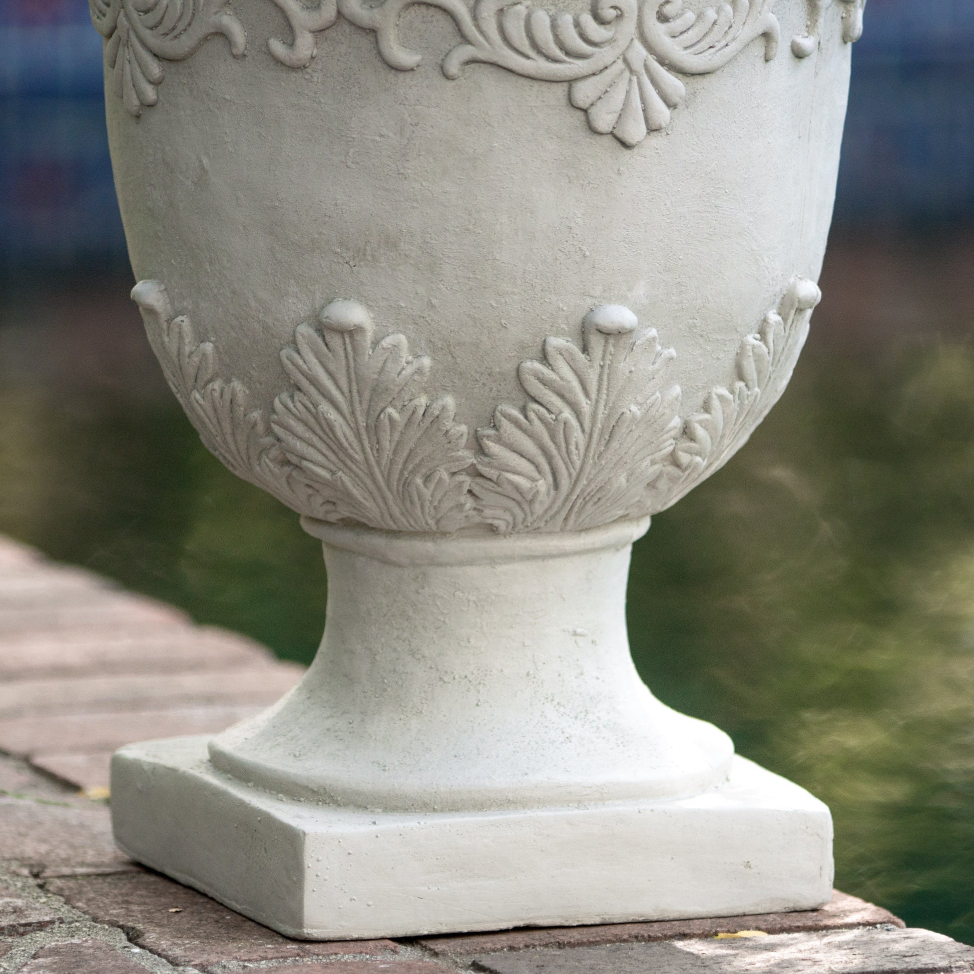 Textured offwhite concrete garden urn with ornate leaf detailing on base
