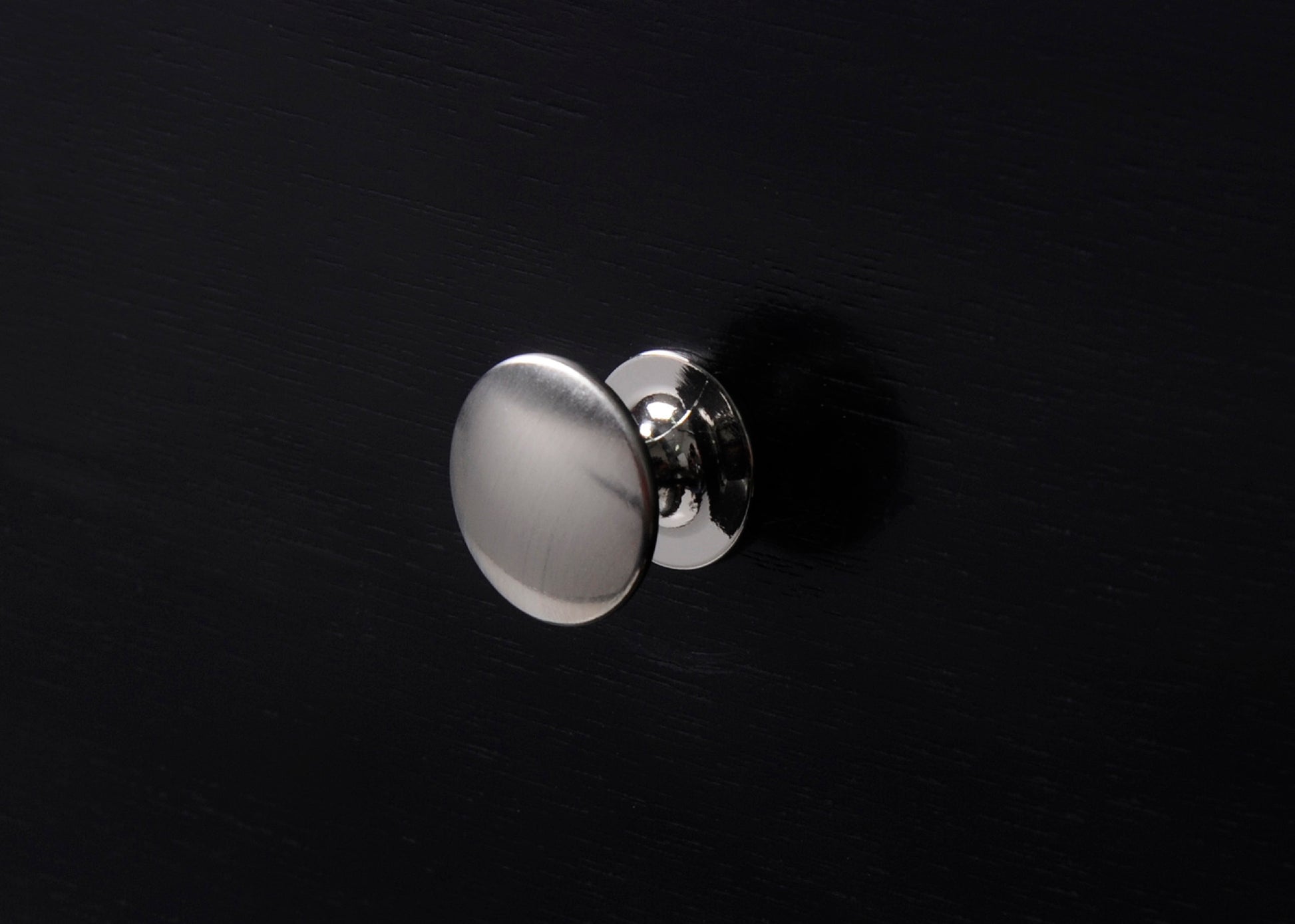 Brushed nickel cabinet knob with a round flat pull on a black surface