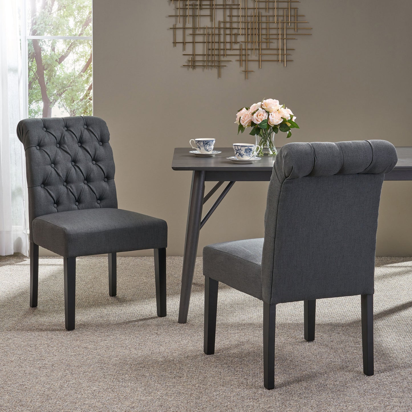 Dark gray tufted dining chairs with rolled backs and black wooden legs