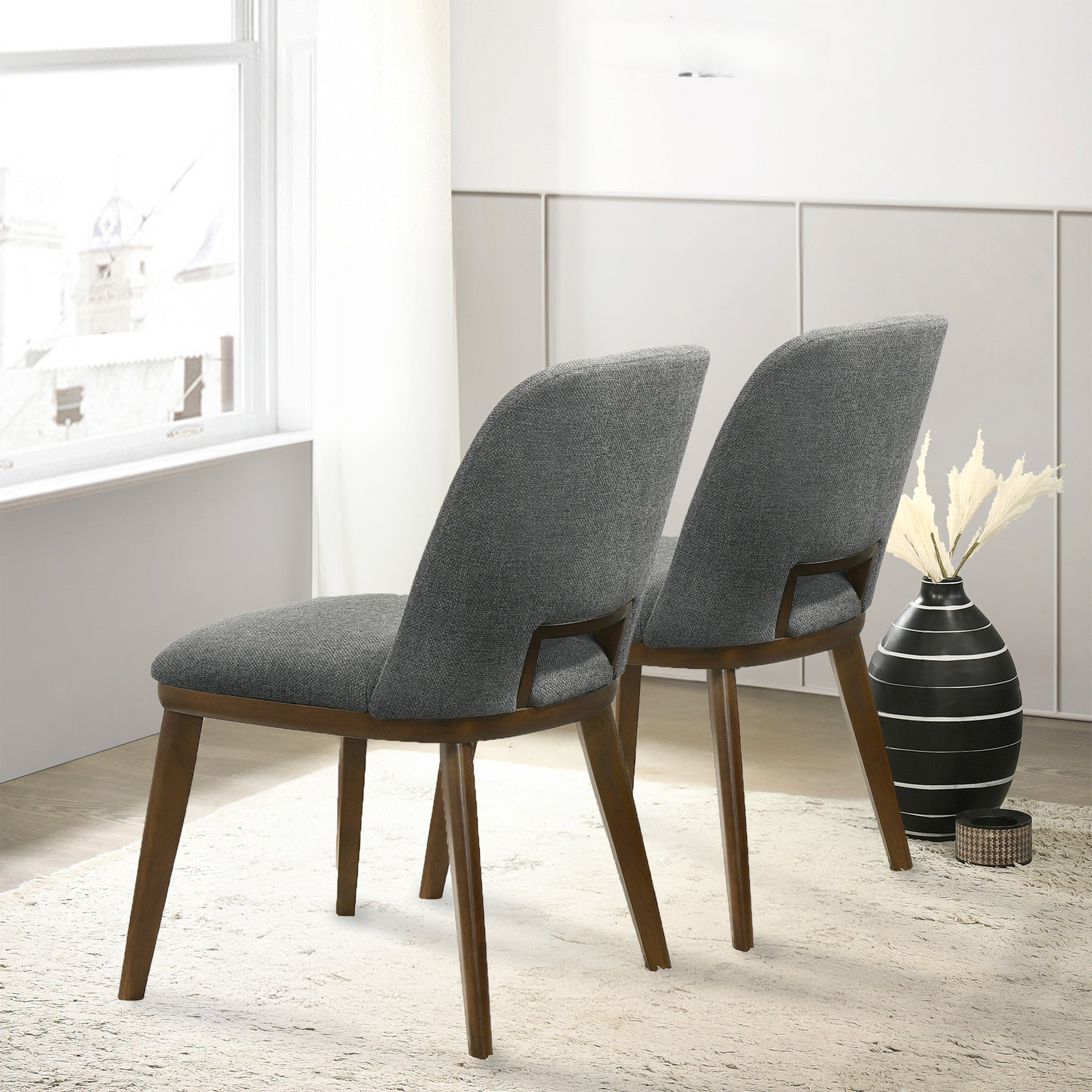 Two grey fabric dining chairs with curved backs and wooden legs set on a cream rug