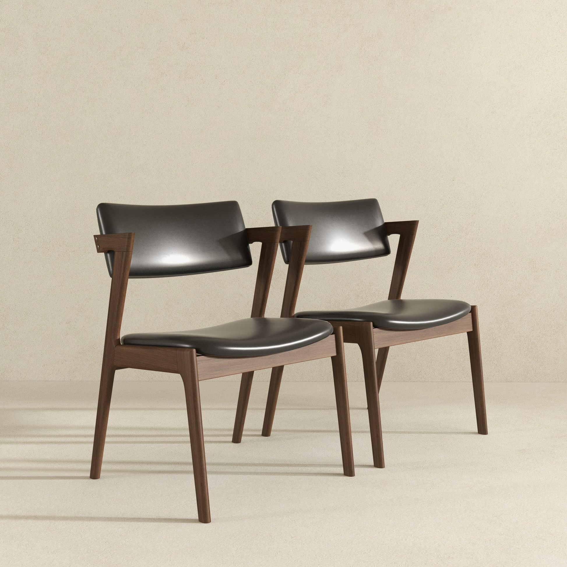 Two modern black leather dining chairs with walnut wood frames featuring sleek curves and tapered legs