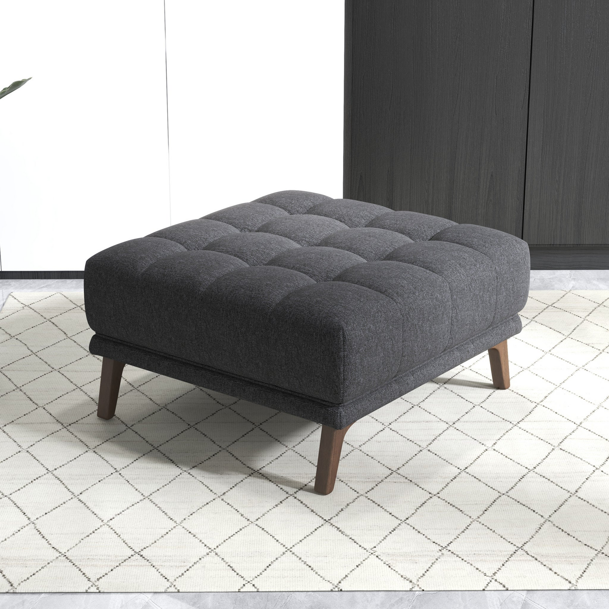 Tufted charcoal grey fabric ottoman with dark wood legs on a diamond patterned rug