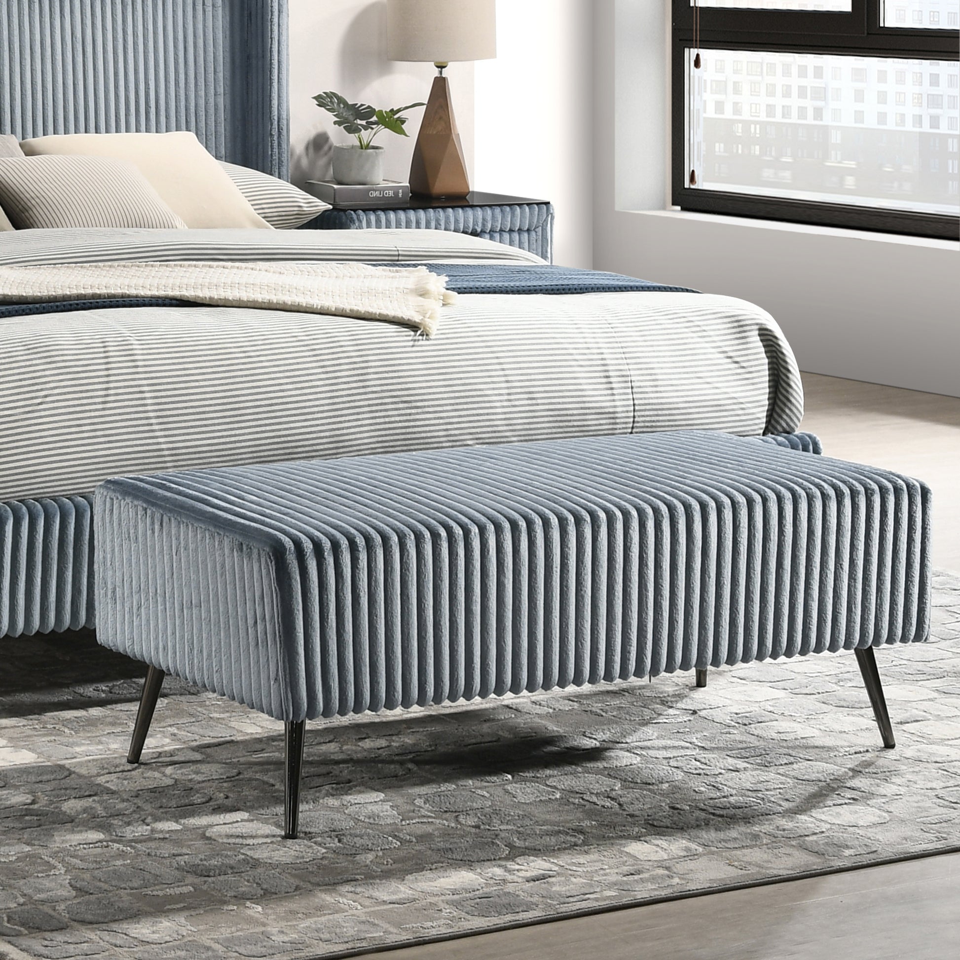 Plush blue velvet ottoman with vertical ribbing and dark metal legs