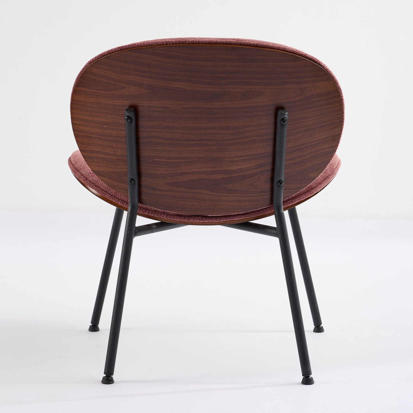 Round rose upholstered chair with a dark wood veneer back and black metal legs