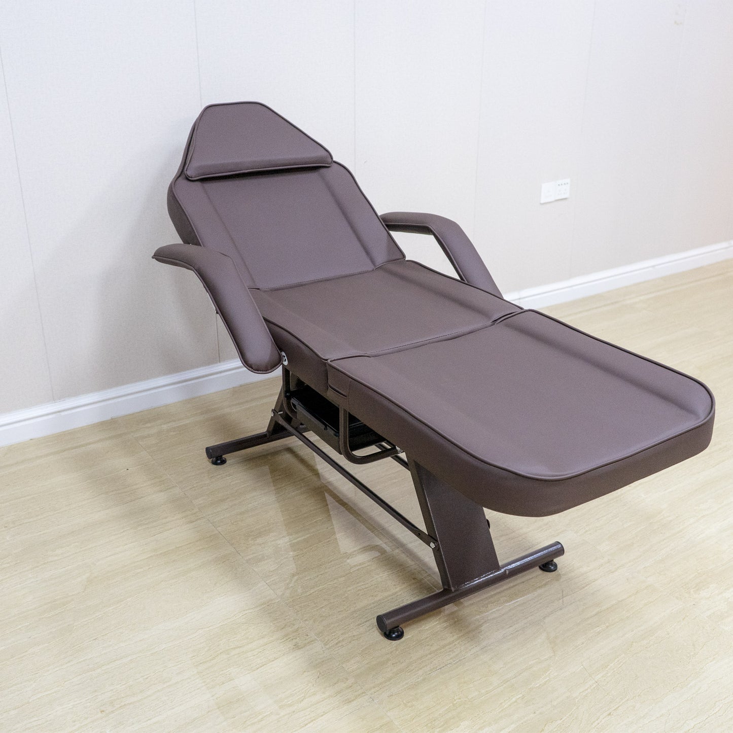 Brown adjustable facial bed with padded headrest and armrests
