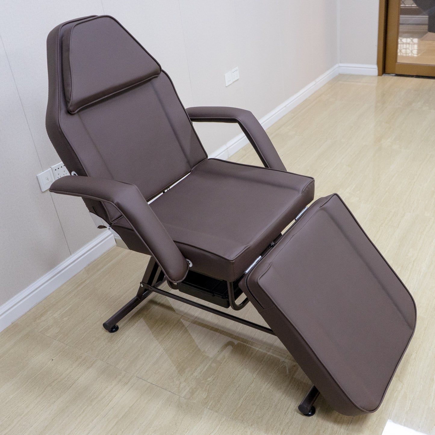 Adjustable brown faux leather facial bed with reclining backrest and footrest for spa treatments