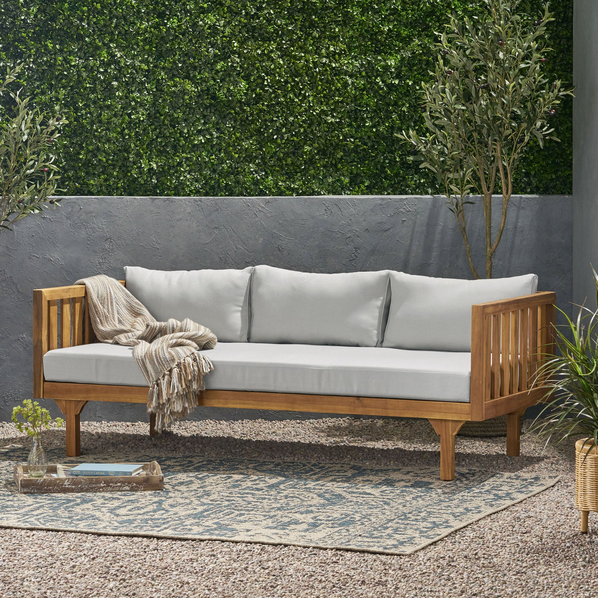 Wooden outdoor couch with light grey cushions and a woven throw