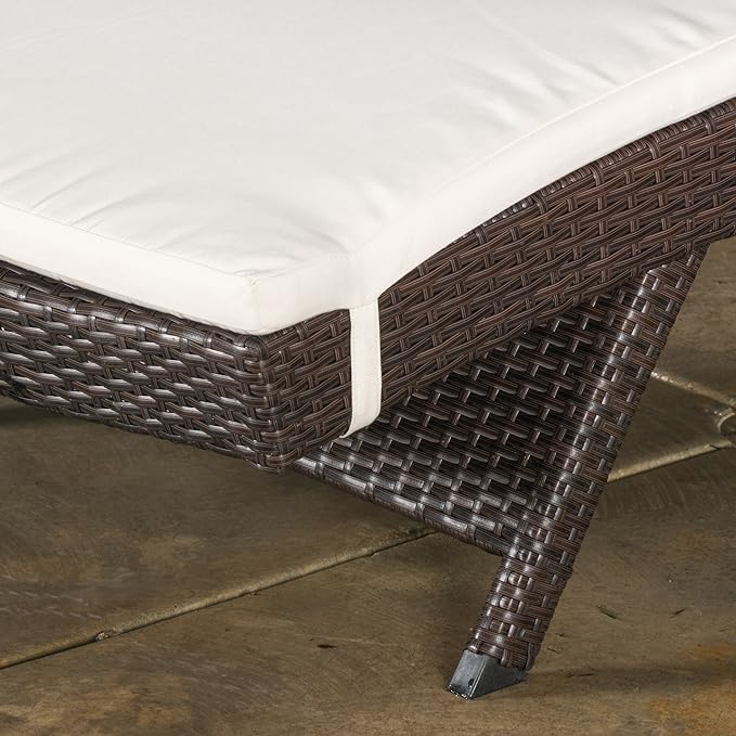 Closeup of dark brown wicker patio chaise lounge with cream cushion and white strap