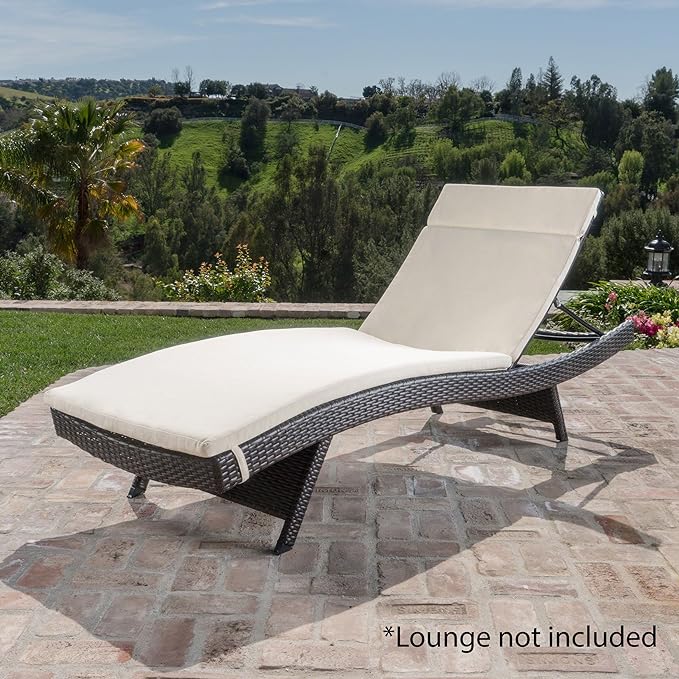Woven brown wicker chaise lounge with a cream cushion on a brick patio