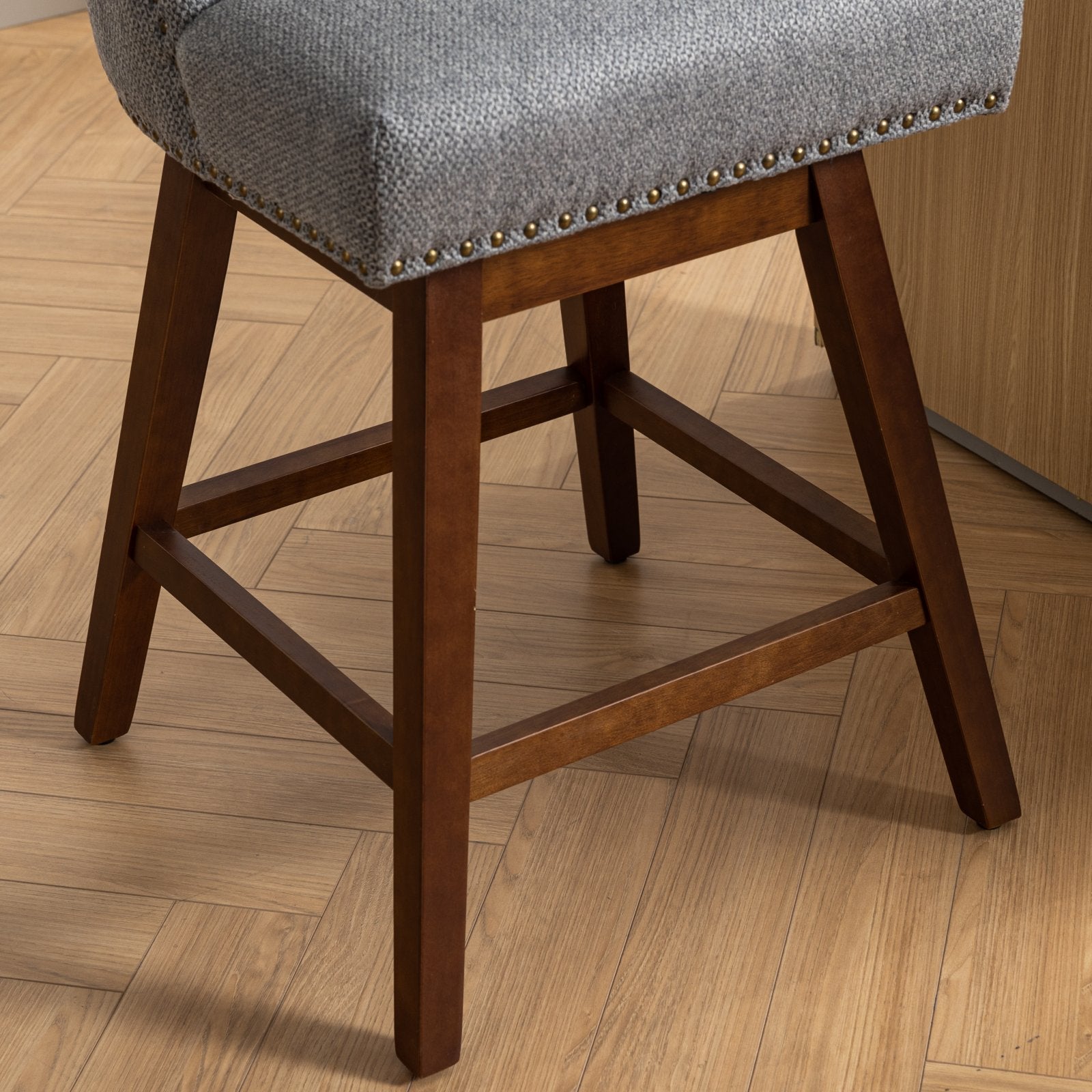 Gray upholstered bar stool with nailhead trim and dark wood legs