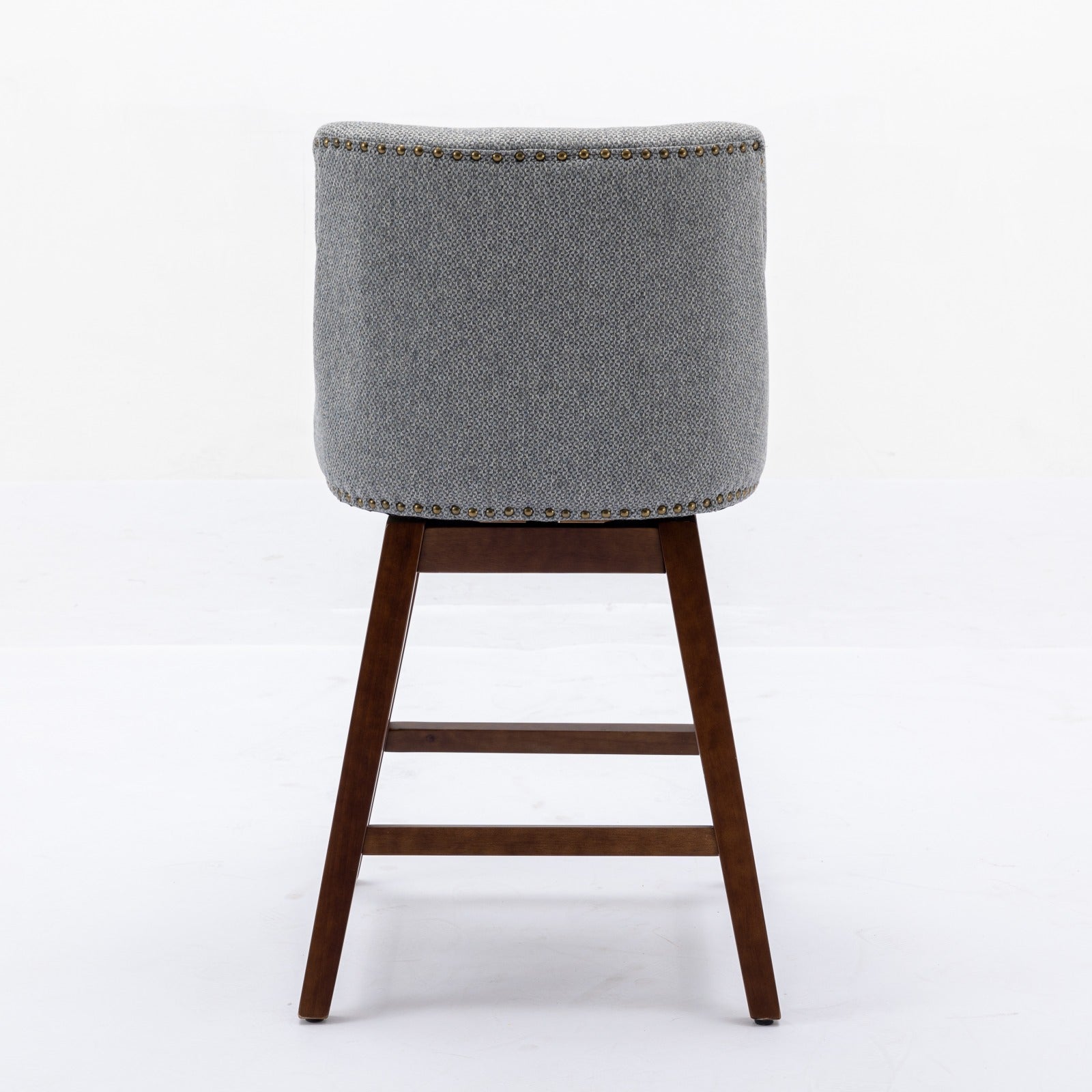 Back view of a grey upholstered swivel bar stool with brass nailhead trim and dark wood legs