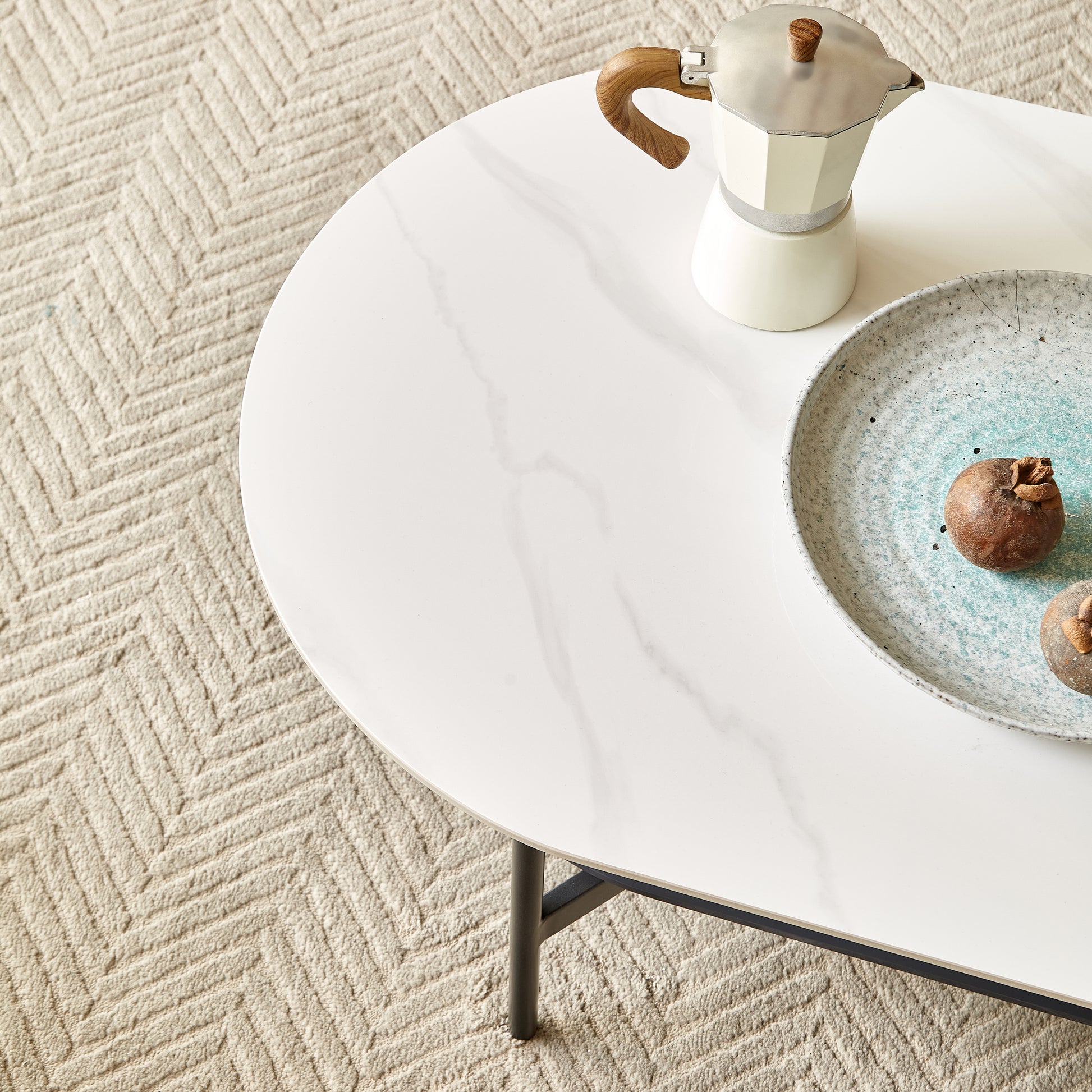White oval coffee table with marbleeffect top and metal legs featuring a moka pot and fruit