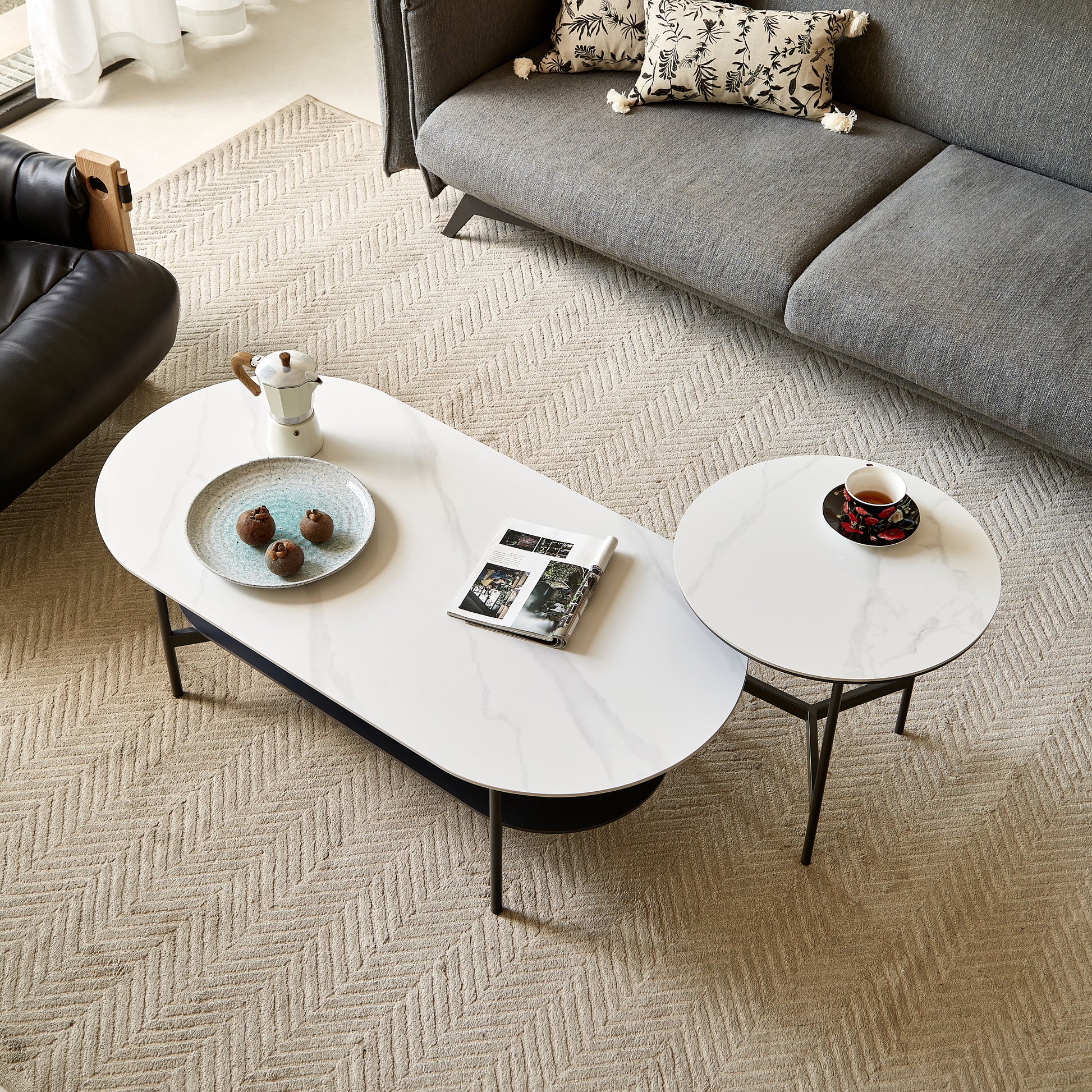 Oval marble effect coffee table with black base holding coffee maker plate of fruit and open magazine