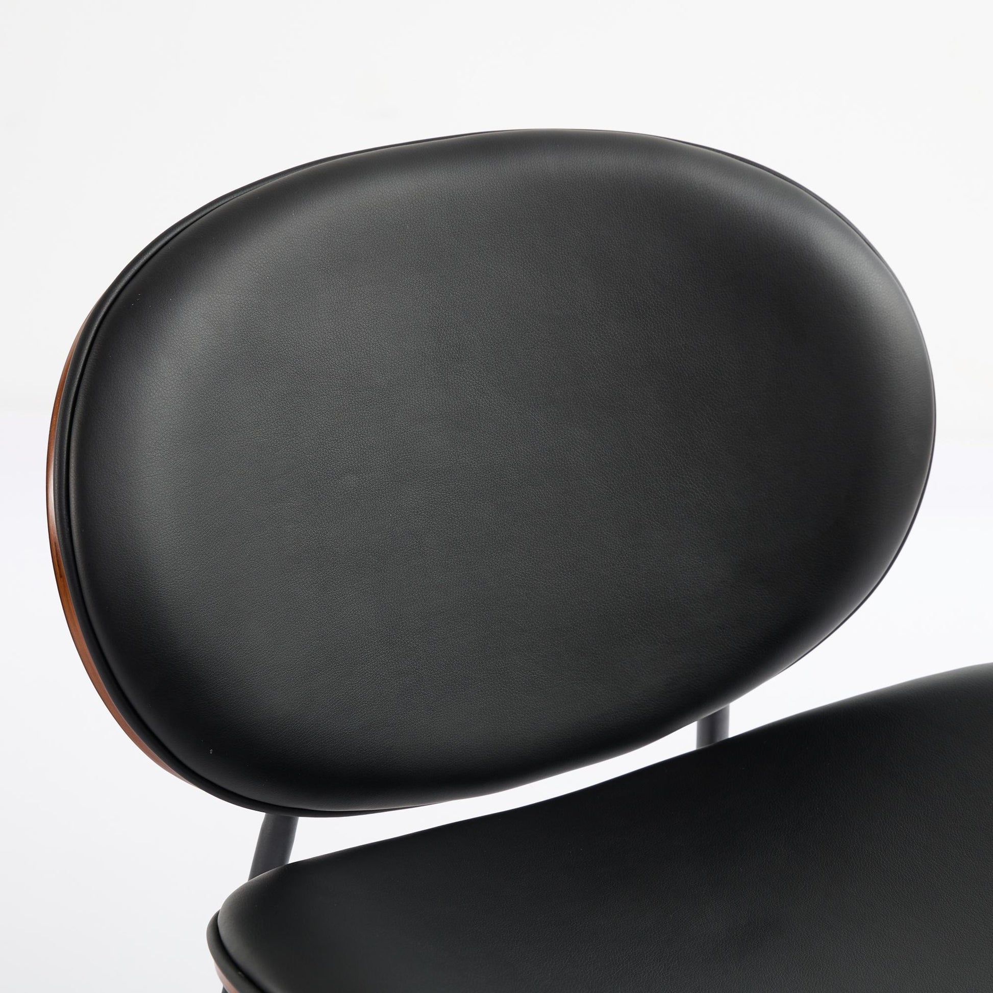 Closeup of a black leather upholstered dining chair with a curved oval backrest and dark wood trim