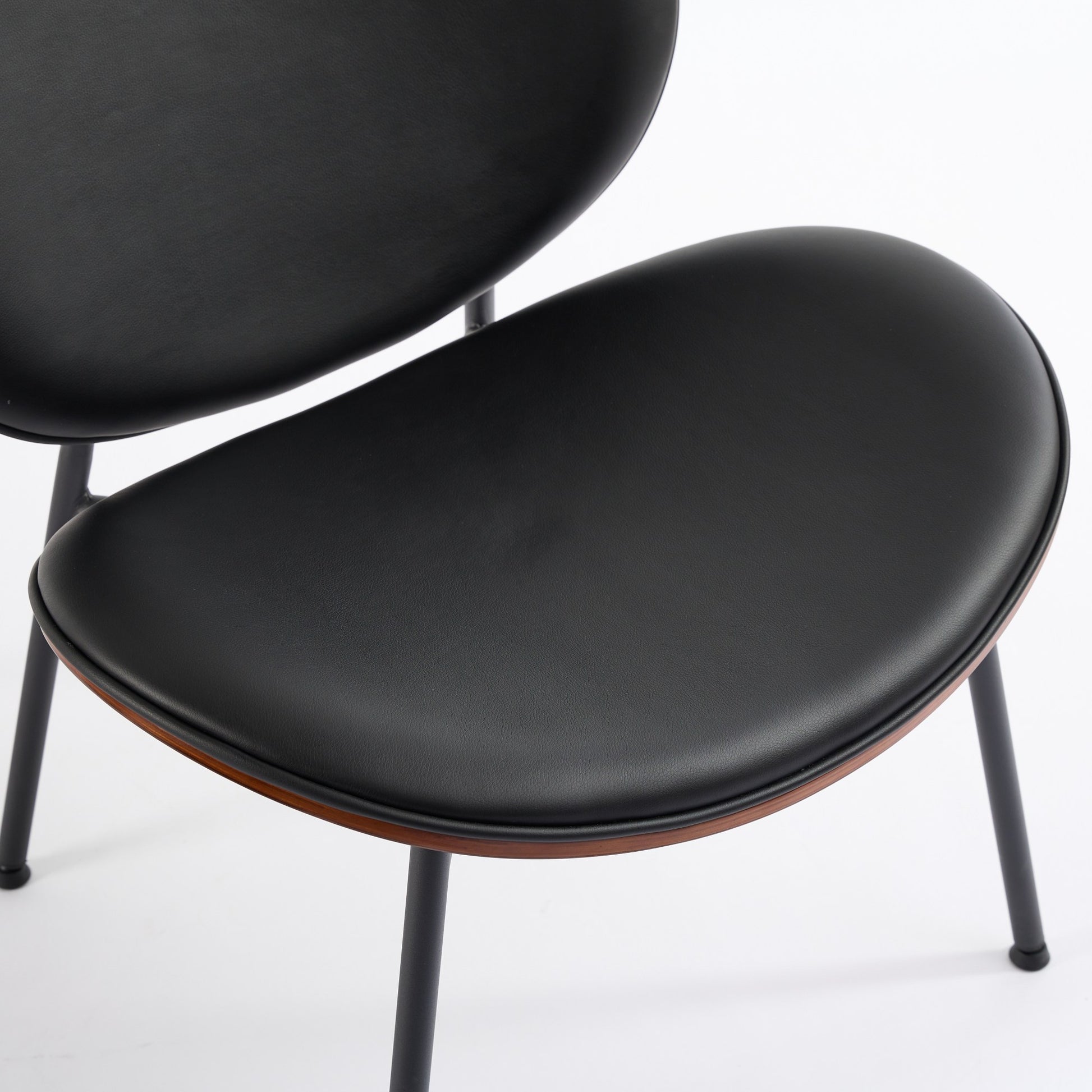 Closeup of a black faux leather dining chair seat with dark wood trim and thin metal legs