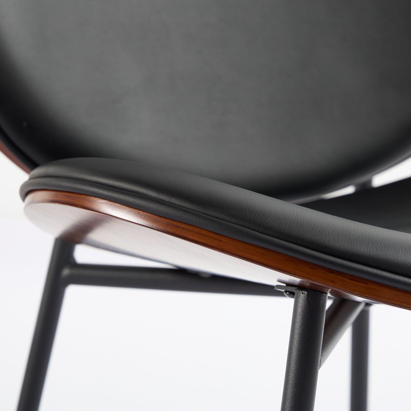 Closeup of black faux leather chair seat with wood trim and metal legs